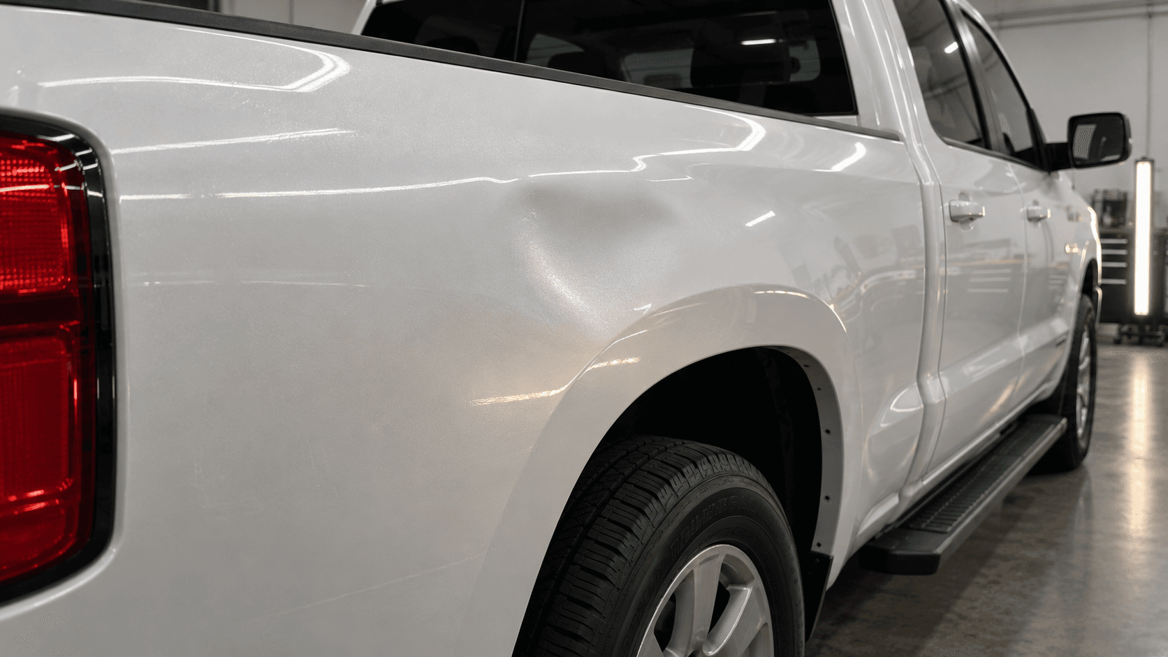 Moderate broad dent on a white pickup bedside before repair